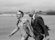 Two grooms walking hand in hand on a beach during their wedding in Cork, Ireland